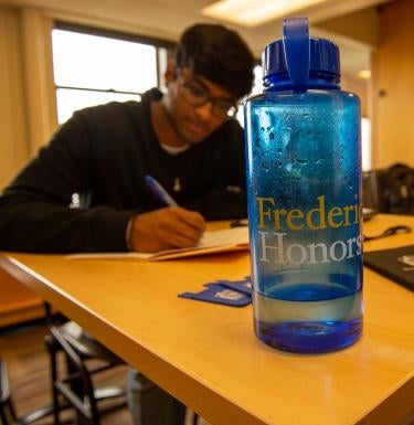 Student studying in the background behind a Frederick Honors College water bottle.