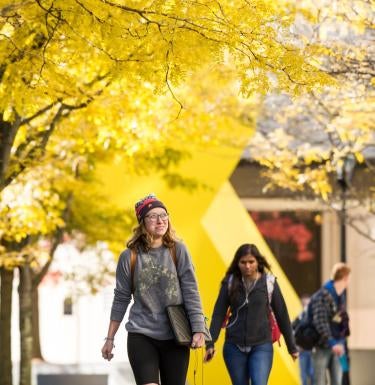 Students walk by large yellow sculpture on Pitt campus