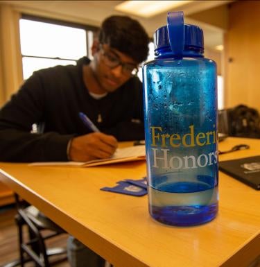Student studying in the background behind a Frederick Honors College water bottle.