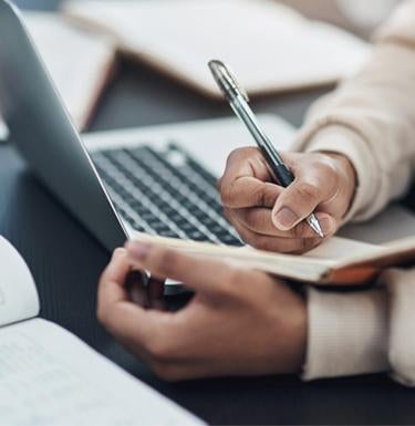 A student takes notes while doing research on a laptop.