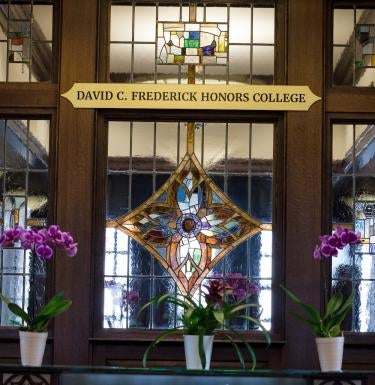 Plaque outside of the Dean's Suite of the David C. Frederick Honors College with stained glass windows and plants.