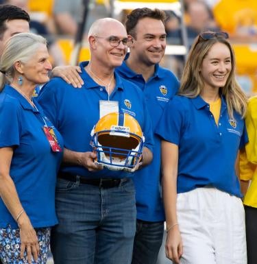 David Frederick holding a football helmet stands along with his wife, Sophie Lynn (second from left), and his family during the Backyard Brawl.